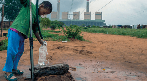 Kind an einem Wasserbrunnen vor dem Kohlekraftwerk Kusile, Südafrika