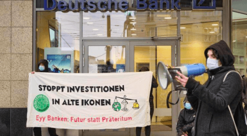 Menschen protestieren vor einer Deutschen Bank Filiale mit einem Banner auf dem steht "Stoppt Investitionen in alte Ikonen"